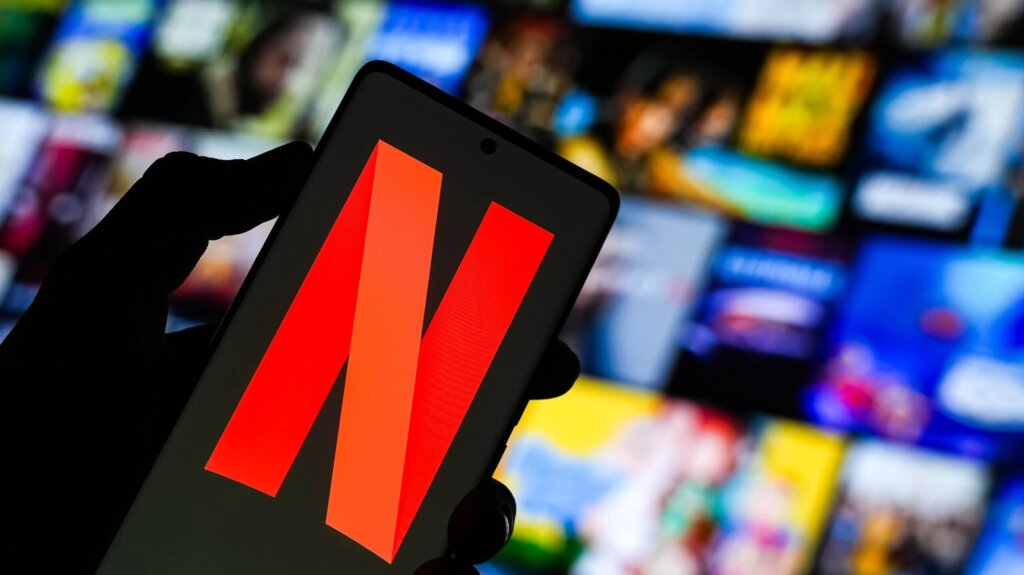 Hand holding smartphone displaying the Netflix logo with a blurred streaming content background