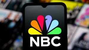 NBC logo displayed on a smartphone screen with blurred colorful background.