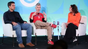 Three people seated on stage in a panel discussion, one wearing a red Phillies shirt and red sneakers.
