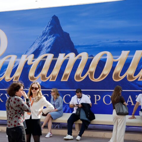 People standing and sitting in front of a large Paramount logo backdrop with a mountain image.