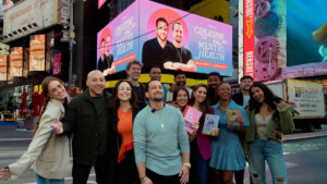 Group of diverse people smiling and holding books in Times Square with a mental health awareness billboard behind them