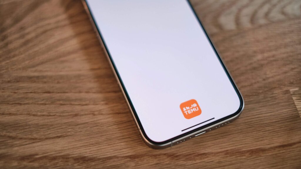 Smartphone displaying the TEMU app logo on a wooden surface.