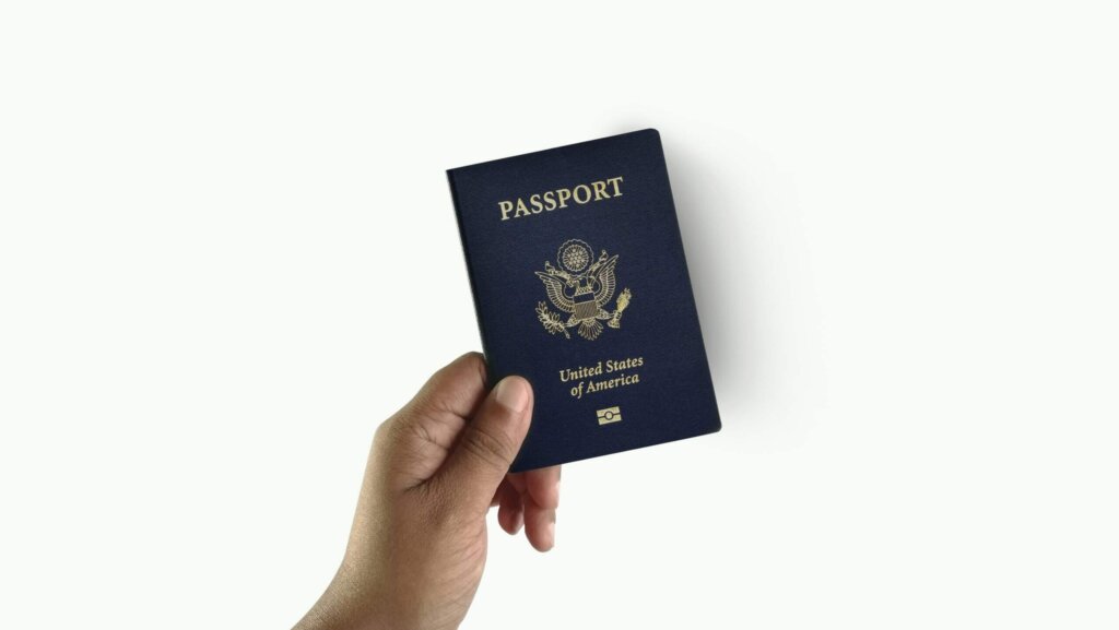 Hand holding a United States of America passport with a dark blue cover and gold emblem.