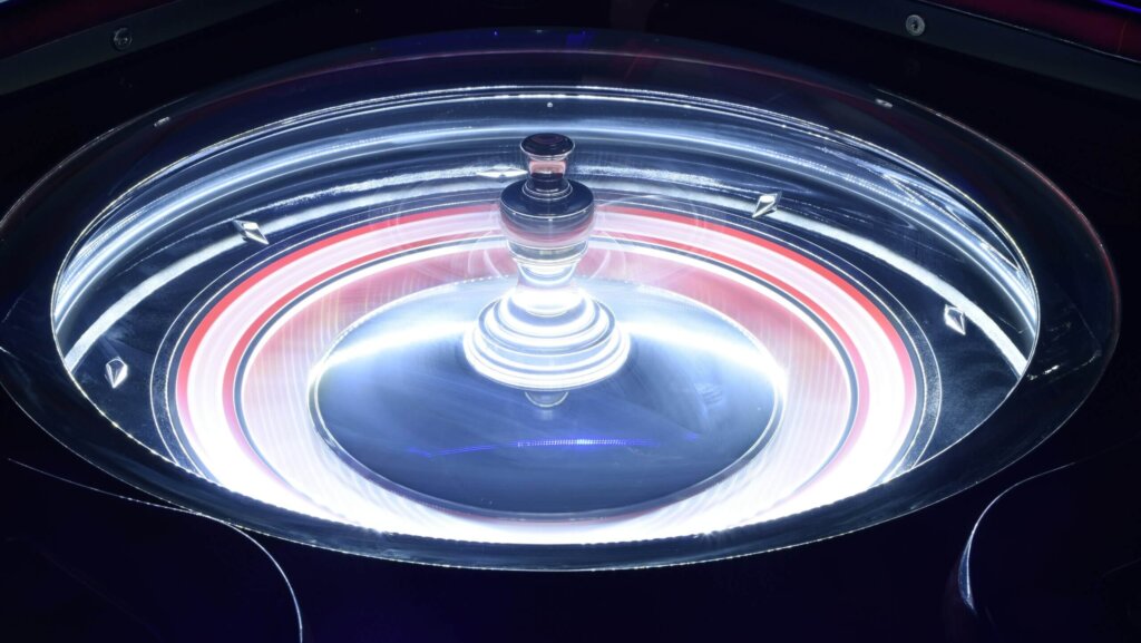 Illuminated roulette wheel spinning with red and white lights in a casino setting.