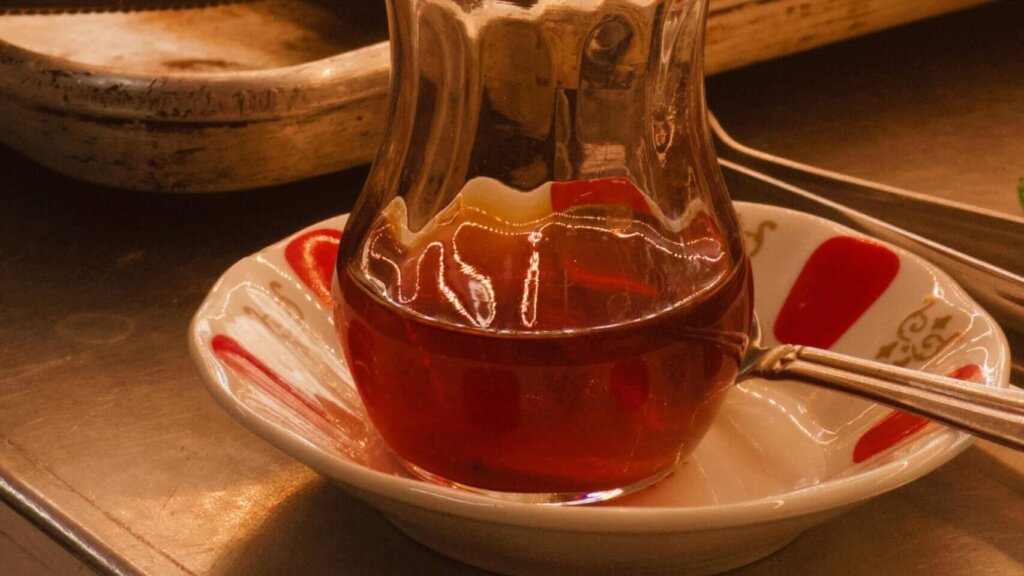 Turkish tea in a tulip-shaped glass on a saucer with assorted baked pastries in the background