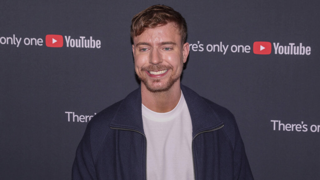Smiling man in a navy jacket and white shirt at a YouTube event with branded backdrop