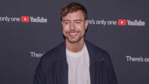 Smiling man in a navy jacket and white shirt at a YouTube event with branded backdrop