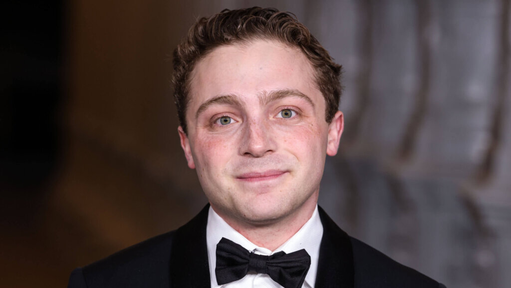 Young man in a black tuxedo and bow tie smiling against a blurred background