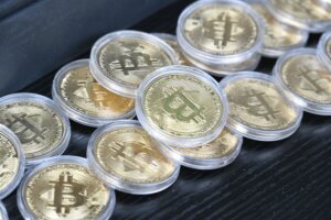 Stacks of gold-colored Bitcoin tokens in clear protective cases on a black surface
