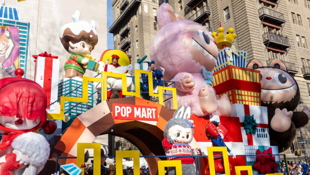 Pop Mart themed parade float with large colorful character balloons and performers in costumes on a city street.