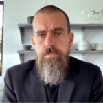 Jack Dorsey with a beard and nose ring speaking in a kitchen setting with shelves of dishes behind him.
