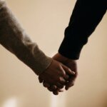 Two people holding hands wearing sweaters against a neutral background