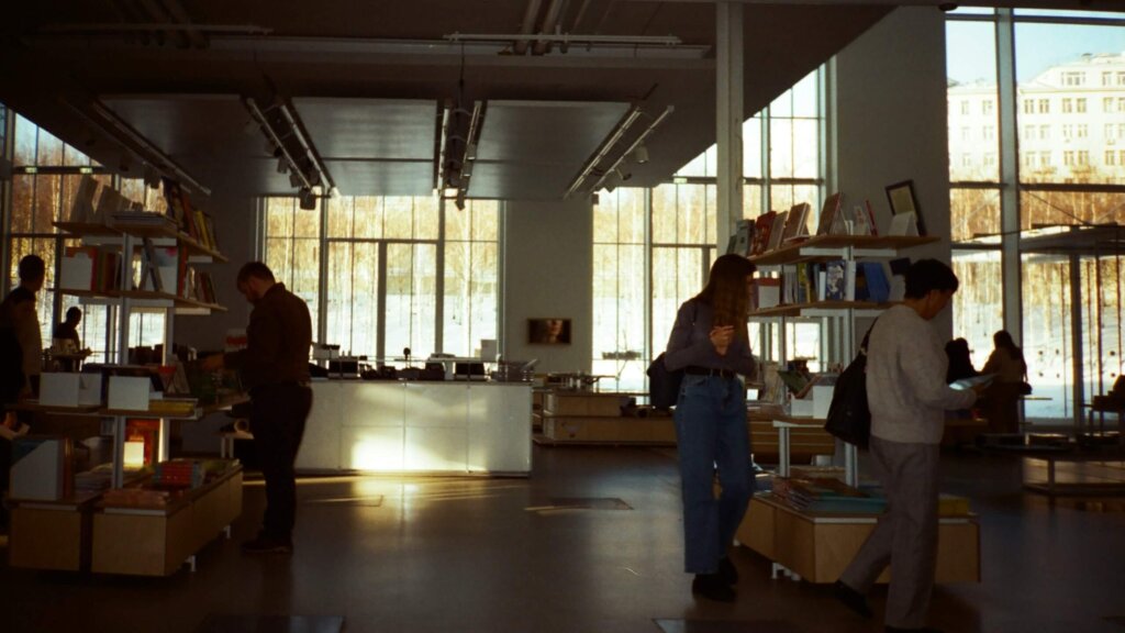 People browsing books in a modern bookstore with large windows and natural light.