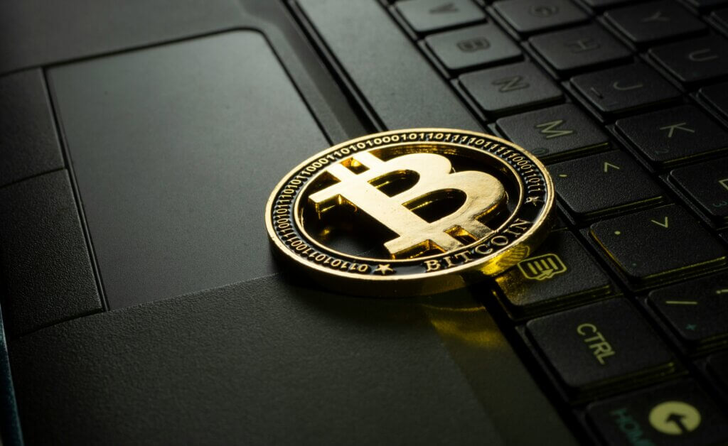 Gold Bitcoin coin resting on a black laptop keyboard near the touchpad and CTRL key