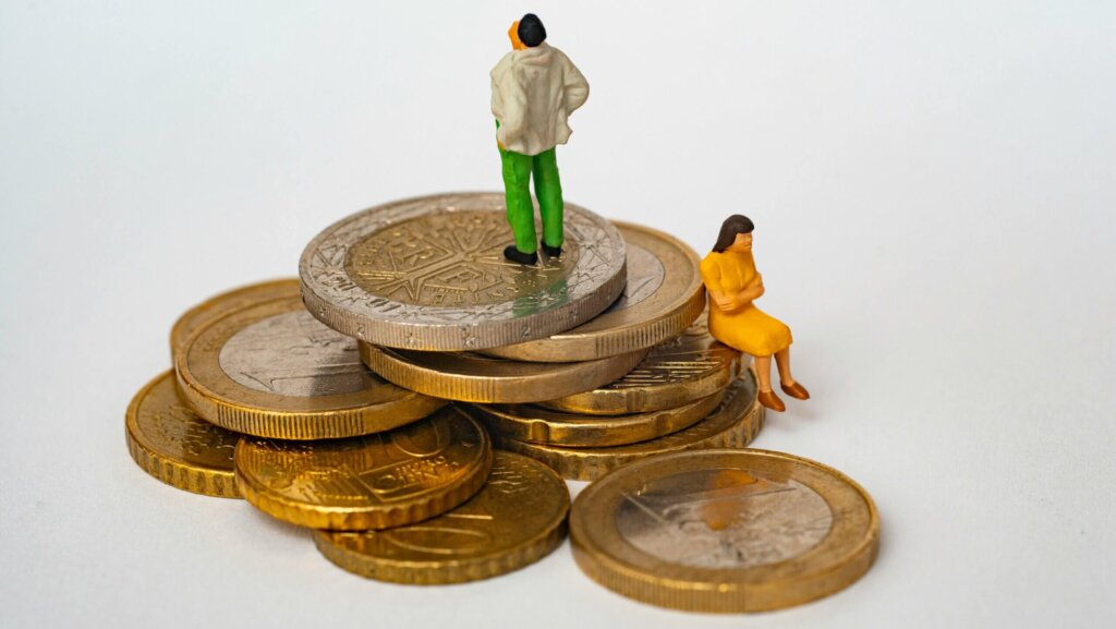 Miniature man standing and woman sitting on stacked Euro coins representing financial disparity