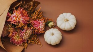 Bouquet of pink and orange flowers next to two small white pumpkins on a brown surface