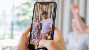 Person recording a man and woman dancing indoors on a smartphone.