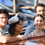 Four young adults smiling and leaning on a wooden boat near a dock with gondolas in the background