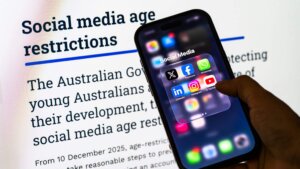 Hand holding smartphone displaying social media apps in front of text about Australian social media age restrictions.