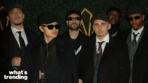 Group of six men wearing dark suits, hats, and sunglasses posing against a green backdrop with "what's trending" text.