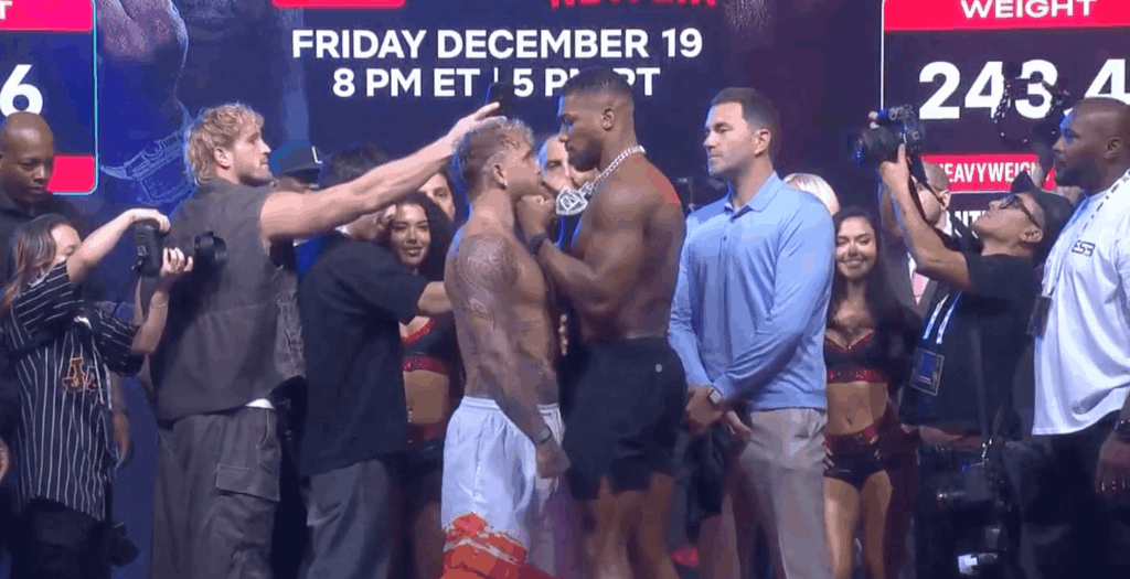 Jake Paul and Tommy Fury face off during a weigh-in event with photographers and spectators around them.