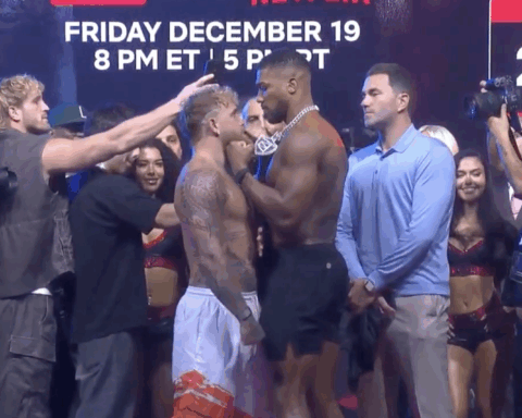 Jake Paul and Tommy Fury face off during a weigh-in event with photographers and officials present.