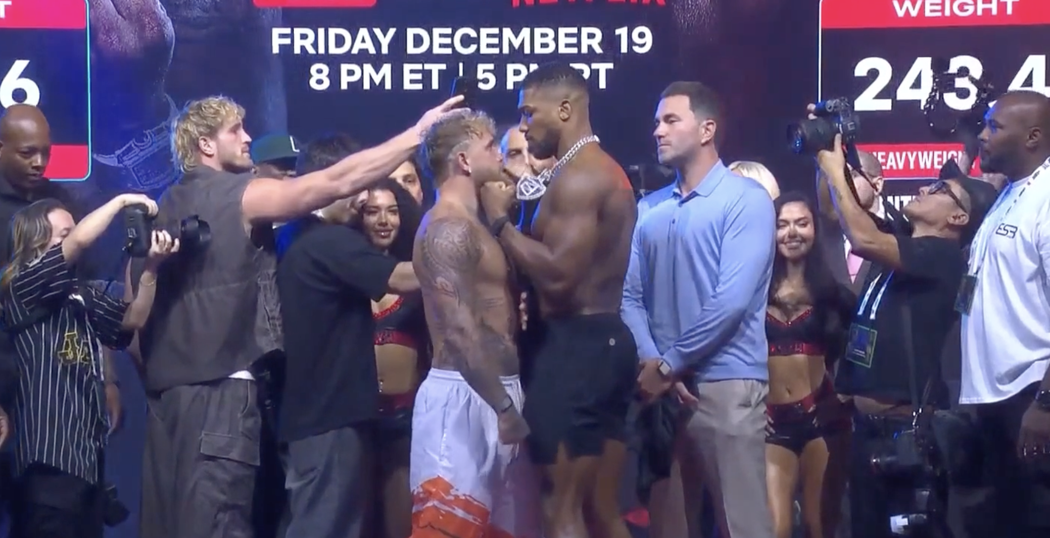 Jake Paul and Tommy Fury face off during a weigh-in event with photographers and officials present.