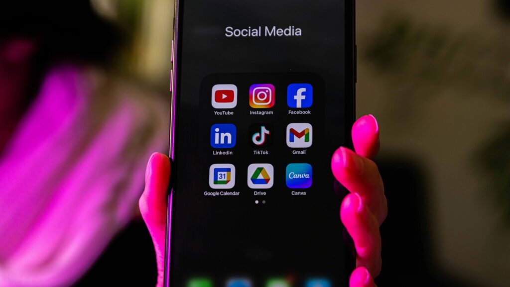 Smartphone screen displaying social media apps including YouTube, Instagram, Facebook, LinkedIn, TikTok, Gmail, Google Calendar, Drive, and Canva.