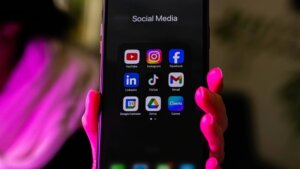 Smartphone screen displaying social media apps including YouTube, Instagram, Facebook, LinkedIn, TikTok, Gmail, Google Calendar, Drive, and Canva.