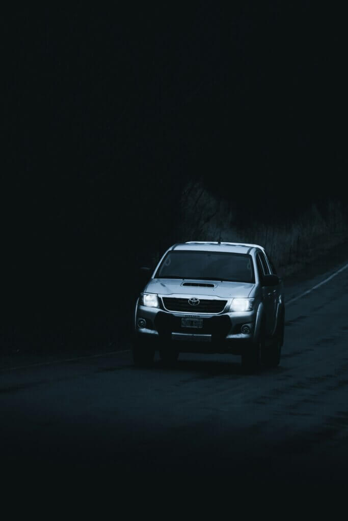 Silver Toyota Hilux driving on a dark road at night with headlights on