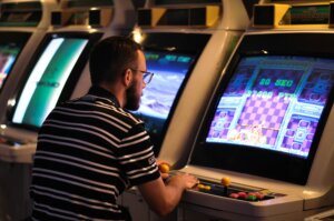 Man in striped Lacoste shirt playing a retro arcade game with joystick and buttons.
