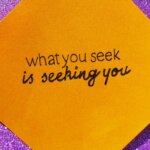 Orange sticky note with the handwritten quote "what you seek is seeking you" on a purple glitter background