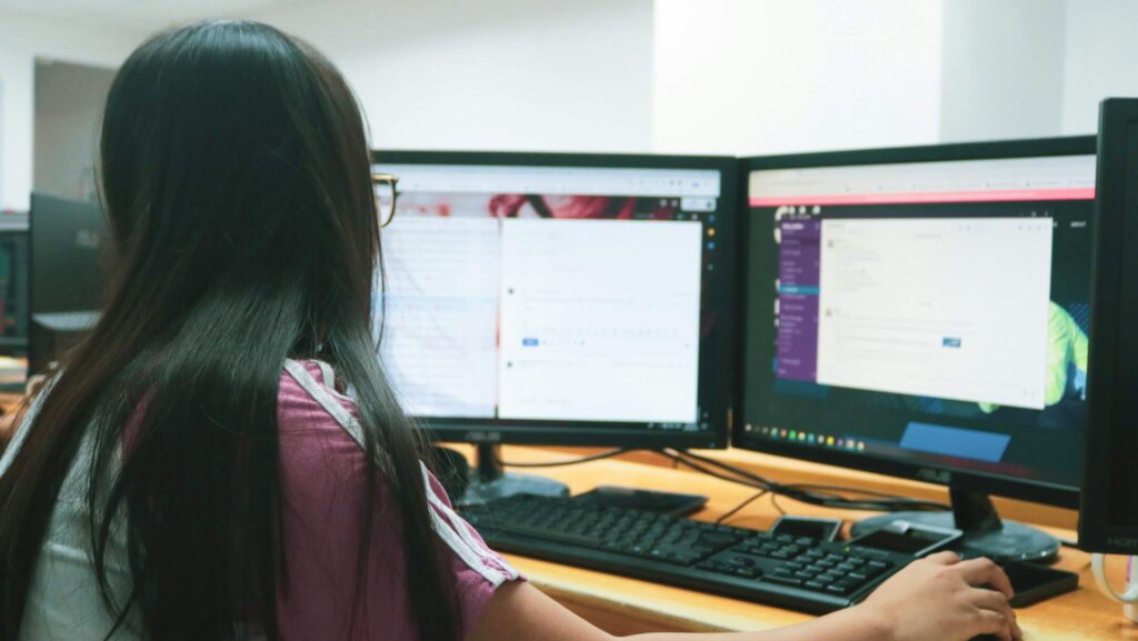 Person with long hair using dual ASUS monitors displaying messaging and email applications at a desk
