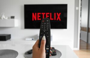 Hand holding TV remote pointed at screen displaying Netflix logo in modern living room.