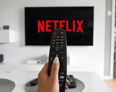 Hand holding TV remote pointed at screen displaying Netflix logo in modern living room.