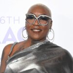 Person with short blonde hair wearing large rhinestone sunglasses and a shiny silver one-shoulder top at the 56th NAACP Awards