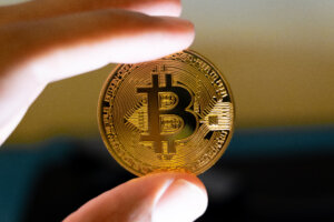 Hand holding a physical gold Bitcoin cryptocurrency coin against a blurred background