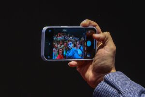 Hand holding smartphone capturing a selfie of a group of people with a large audience in the background.