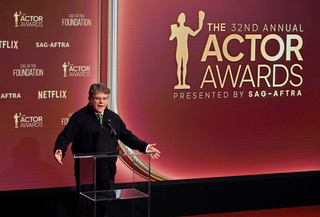 Man speaking at podium during the 32nd Annual Actor Awards presented by SAG-AFTRA with Netflix branding visible