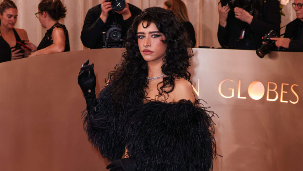 Woman with curly hair wearing a black feathered off-shoulder top and wide-leg pants on a red carpet at the Golden Globes