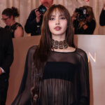 Lisa of BLACKPINK wearing a sheer black gown with a gold choker on the red carpet at the Golden Globes