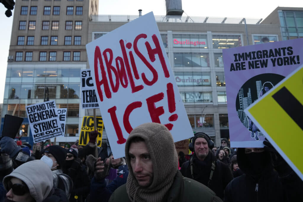 Protesters holding signs including "Abolish ICE!" and "Immigrants Are New York!" in an urban setting.