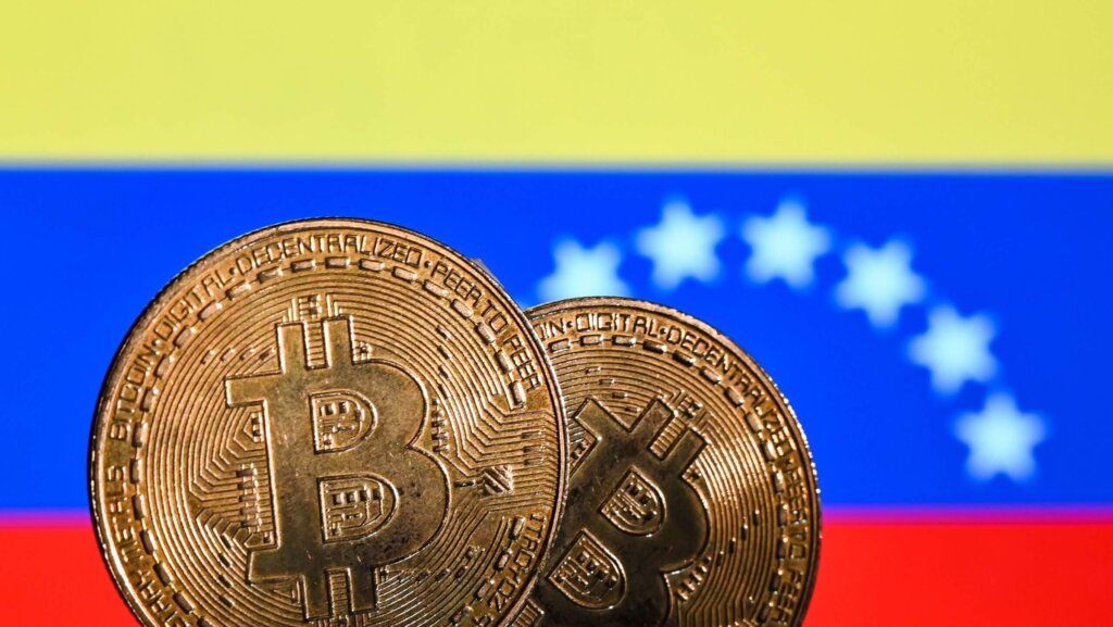 Two Bitcoin coins in front of the Venezuelan flag with yellow, blue, and red stripes and white stars
