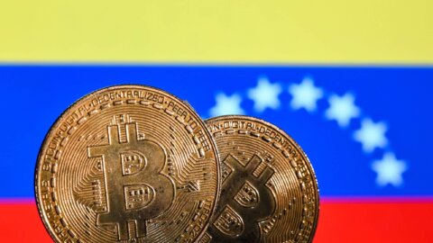 Two Bitcoin coins in front of the Venezuelan flag with yellow, blue, and red stripes and white stars