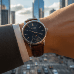 Close-up of a wrist wearing a Quecmatic Borante watch with a brown leather strap in an urban setting.