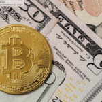 Gold Bitcoin coin on top of US dollar bills including a five-dollar bill with Alexander Hamilton's portrait