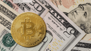 Gold Bitcoin coin on top of US dollar bills including a five-dollar bill with Alexander Hamilton's portrait