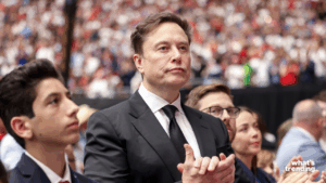 Elon Musk in a black suit and tie clapping at a crowded event.
