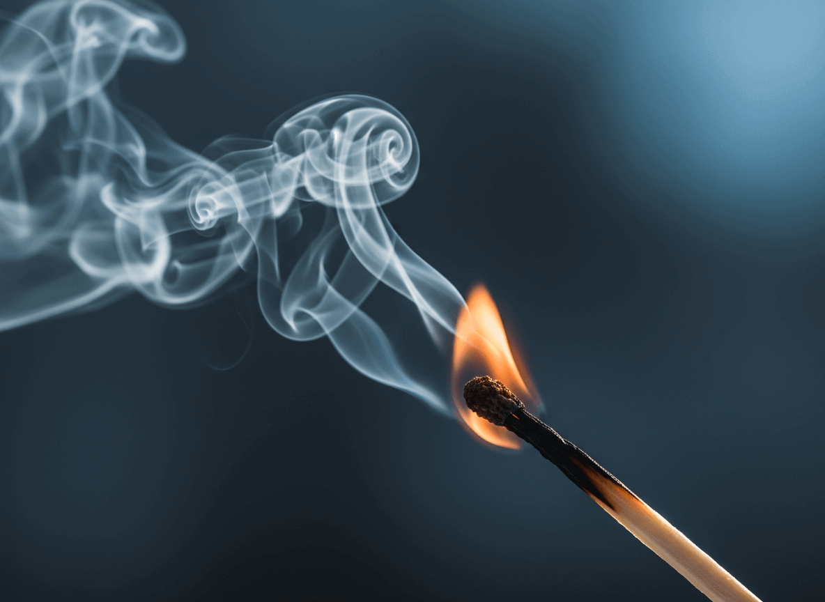 Close-up of a burning matchstick with curling smoke against a dark background