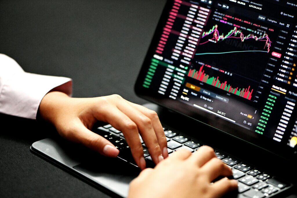 Hands typing on a laptop keyboard displaying Binance cryptocurrency trading charts and data